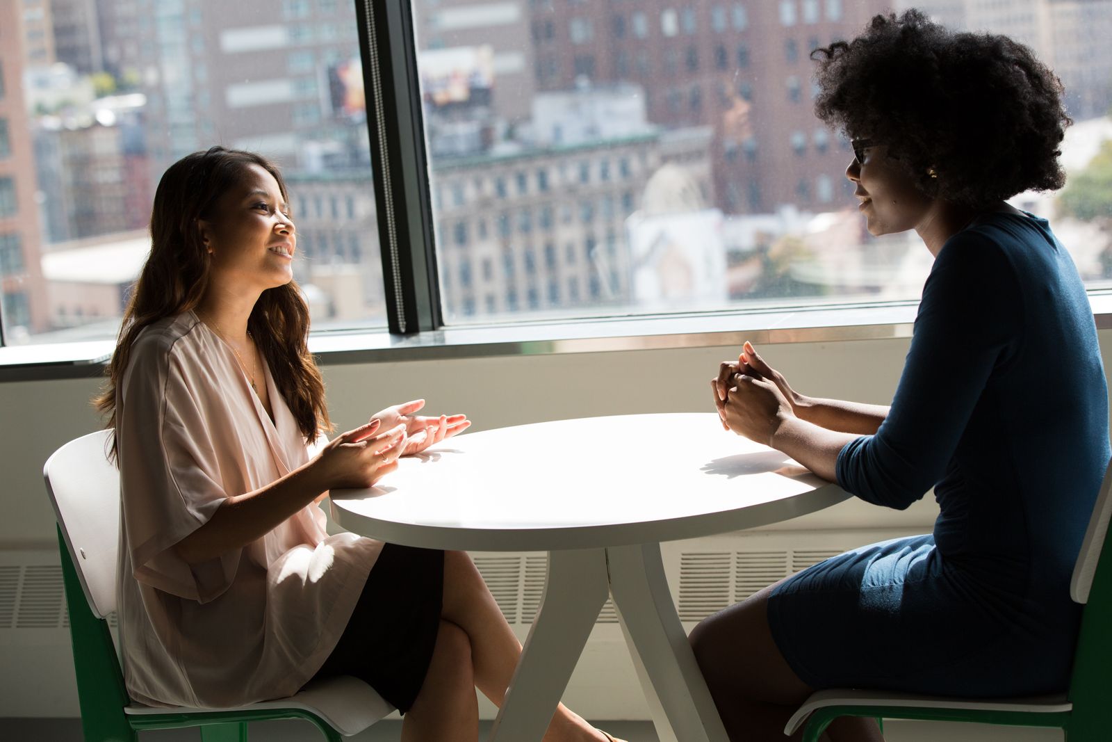 Duas mulheres conversam sentadas em uma mesa redonda com vista para a cidade.