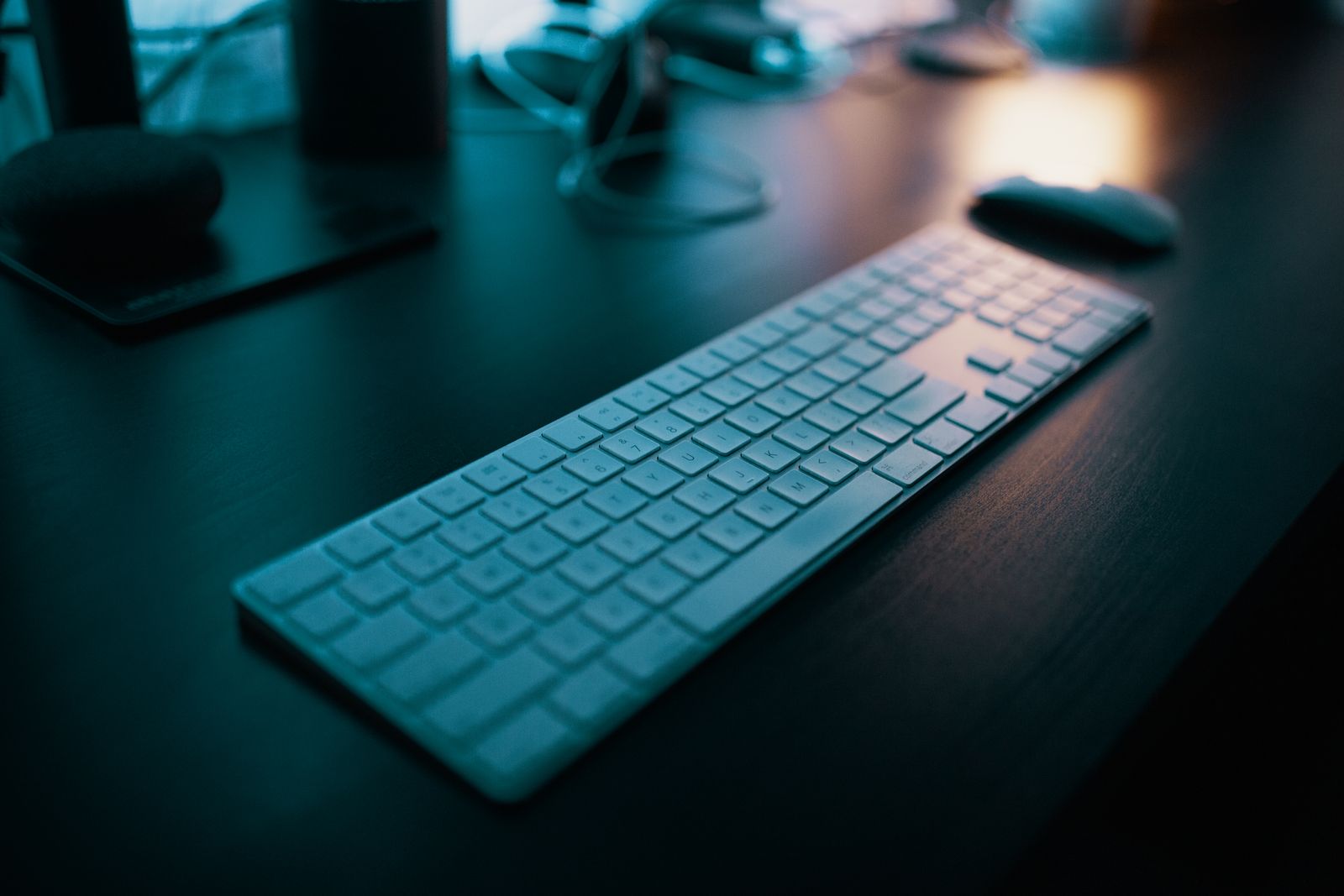 Teclado e mouse sobre uma mesa escura em um escritório com pouca luz.